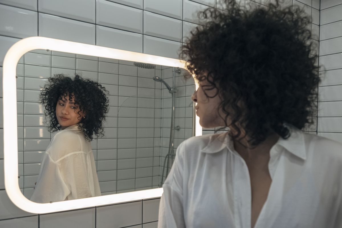 Young Woman With Dark Curly Hair Checking Clothes In The Mirror