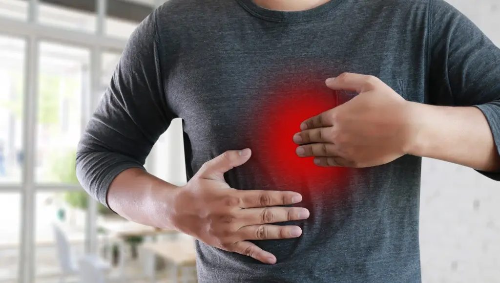 A person holding their chest and abdomen, with a red glow on the chest area, indicating pain or discomfort.