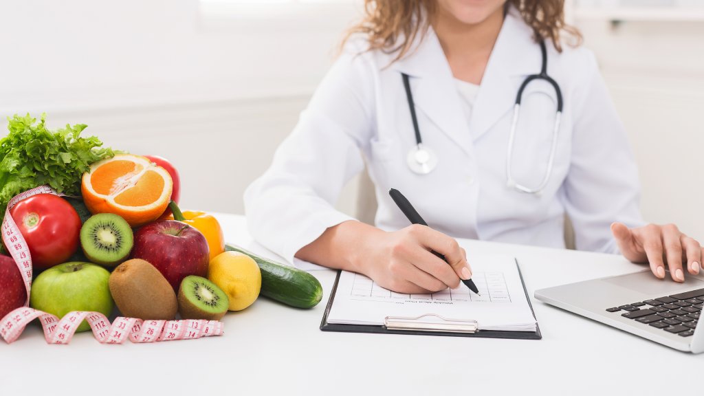 Doctor writing diet plan on table and using laptop, panorama, copy space
