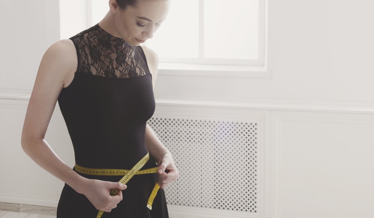 Beautiful woman in black with measuring tape in light hall. Slimming and weight loss concept.