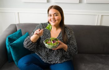 Beautiful latin woman eating a healthy green salad. Fat young woman on a diet trying to lose some weight