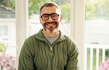 Portrait, mature and happy man in house for relax, peace and calm on weekend break with good mood. Glasses, smile and person chill in home for staycation, wellness and confidence in Australia